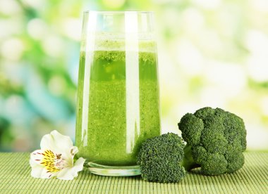 Bir bardak brokoli suyu, bambu hasırında, yeşil arka planda.