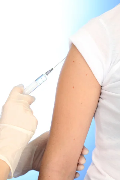 Arts bedrijf spuit met een vaccin in de patiënt schouder, op blauwe achtergrond — Stockfoto