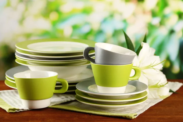 Empty plates and cups on wooden table on green background — Stock Photo, Image