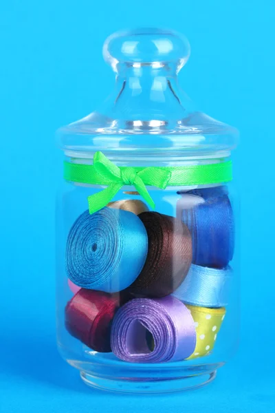Pot en verre contenant divers rubans colorés sur fond bleu — Photo