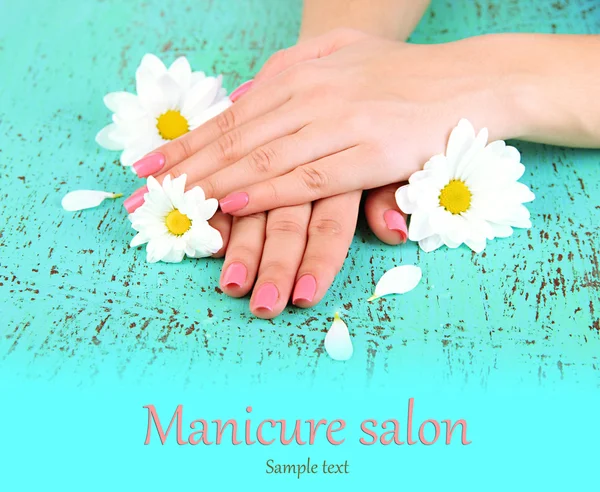 Vrouw handen met roze manicure en bloemen, op een achtergrond met kleur — Stockfoto