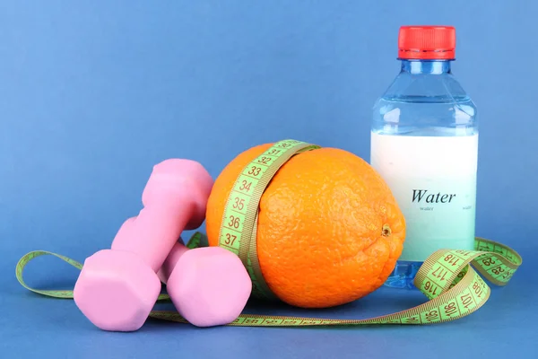 Oranje met het meten van tape, halters en fles water, op een achtergrond met kleur — Stockfoto