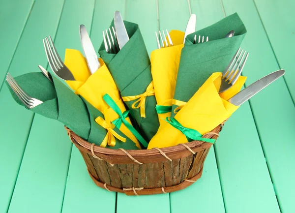 Tenedores y cuchillos envueltos en servilletas de papel verde y amarillo, sobre fondo de madera de color —  Fotos de Stock