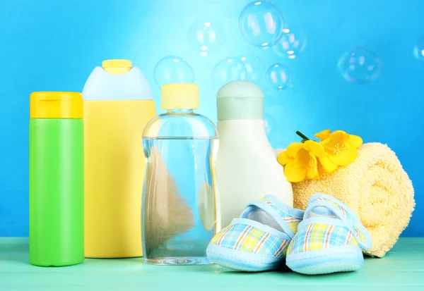 Cosméticos para bebés, toallas y botas sobre mesa de madera, sobre fondo azul — Foto de Stock