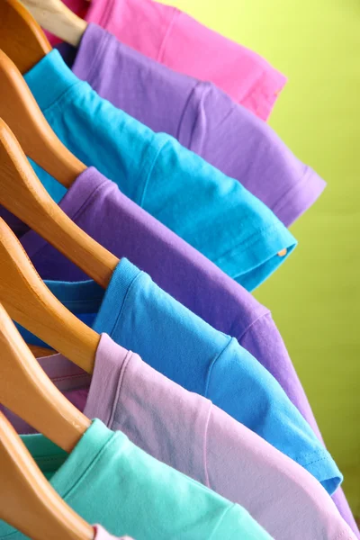 Veel t-shirts op hangers op groene achtergrond — Stockfoto