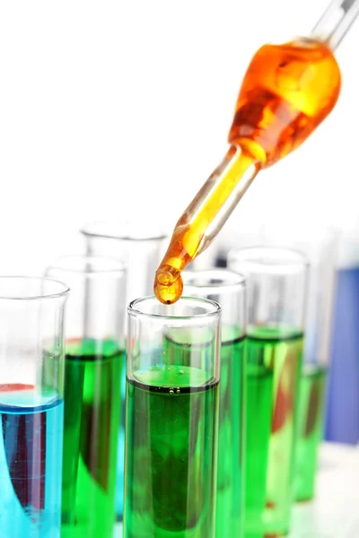 Pipeta de laboratorio con gota de líquido de color sobre tubos de ensayo de vidrio, de cerca, aislado en blanco — Foto de Stock