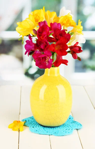 Beautiful bouquet of freesia in blue vase on wooden table on window background — Stock Photo, Image