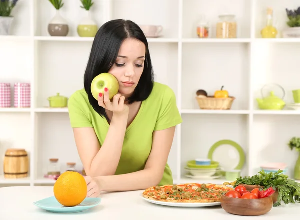 Pretty girl selecciona pizza o dieta en el fondo de la cocina — Foto de Stock