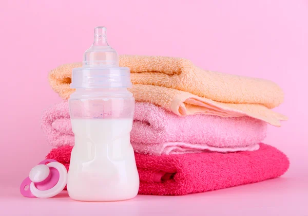 Botella para leche con toallas y pezón sobre fondo rosa —  Fotos de Stock