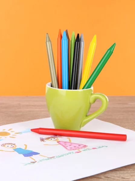 Colorful pencils in cup on table on orange background