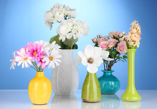 Hermosas flores en jarrones sobre fondo azul — Foto de Stock