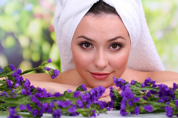 Mulher bonita com toalha na cabeça e flores no fundo brilhante — Fotografia de Stock