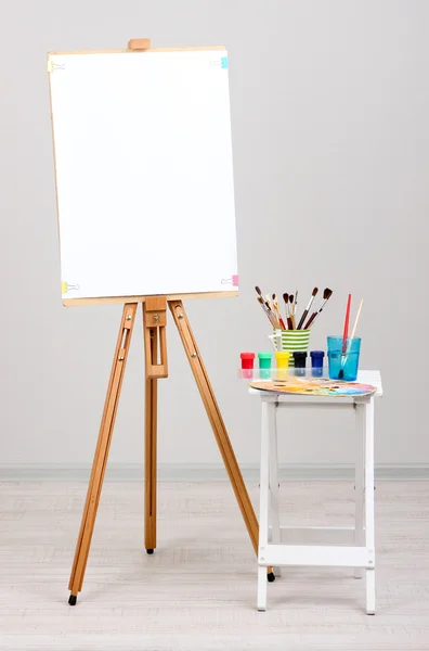 Wooden easel with clean paper and art supplies in room — Stock Photo, Image