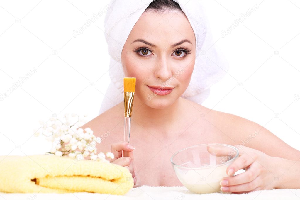 Beautiful young woman with cream for face mask and towel on her head isolated on white