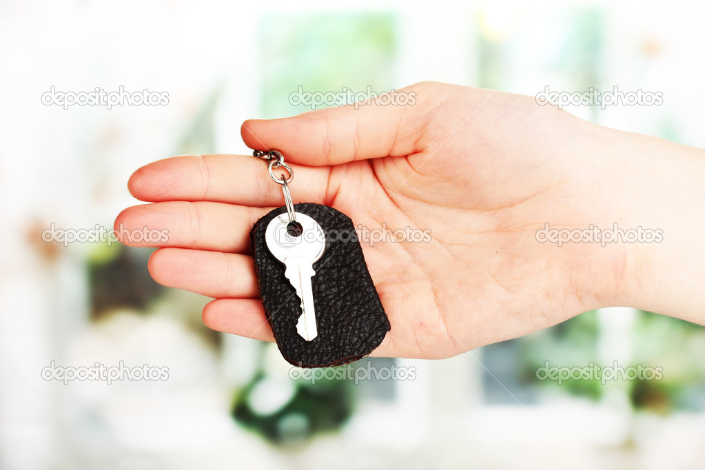 Key with leather trinket in hand on window background