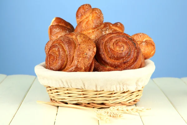 Composition with buns in wicker basket, on wooden table, on color background — Stock Photo, Image