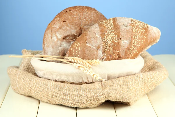 Bread in wicker basket, on wooden table, on color background — Stock Photo, Image