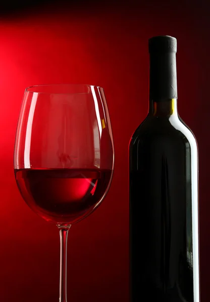 Μπουκάλι και το ποτήρι του κρασιού σε κόκκινο φόντο — Φωτογραφία Αρχείου