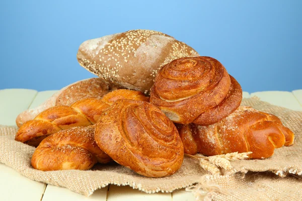 Composizione con pane, rotoli su sacco, su tavolo di legno, su sfondo a colori — Foto Stock