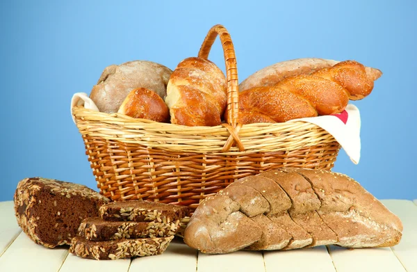 Složení s chlebem a rohlíky, v proutěném koši na dřevěný stůl, na barvu pozadí — Stock fotografie