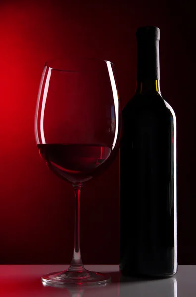 Sklenka vína s lahví na zářivě červeném pozadí — Stock fotografie