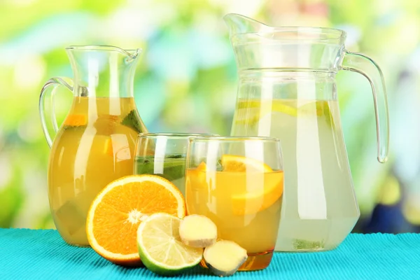 Limonada de laranja e limão em jarros e copos em mesa de madeira sobre fundo natural — Fotografia de Stock