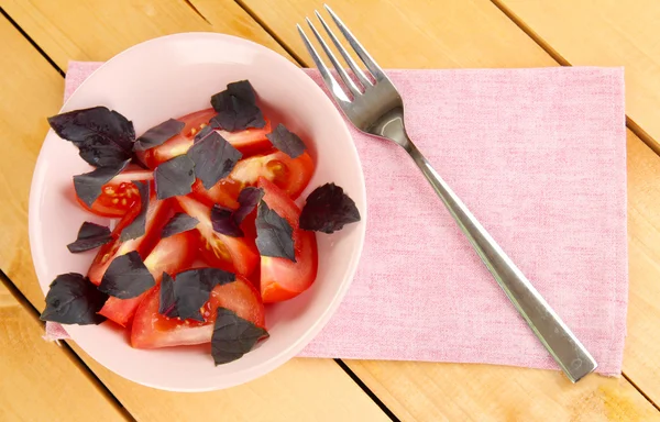 Sallad på färska tomater med basilika bladen i en skål på servett på trä bakgrund — Stockfoto