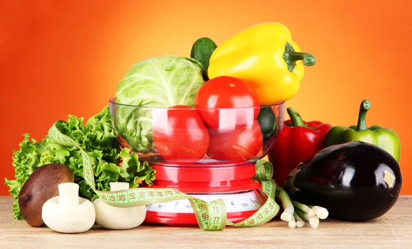 Fresh vegetables in scales on table on orange background — Stock Photo, Image