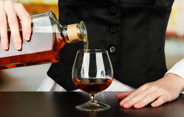 Barman hand with bottle of cognac pouring drink into glass, on bright background — Stock Photo, Image