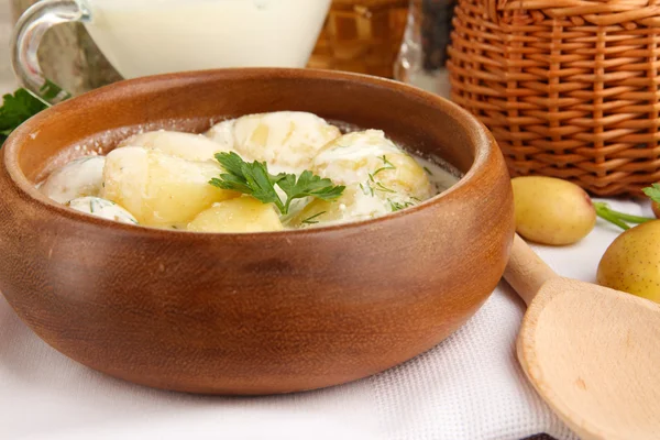 Tender young potatoes with sour cream and herbs in wooden bowl on tablecloth close-up — Stock Photo, Image