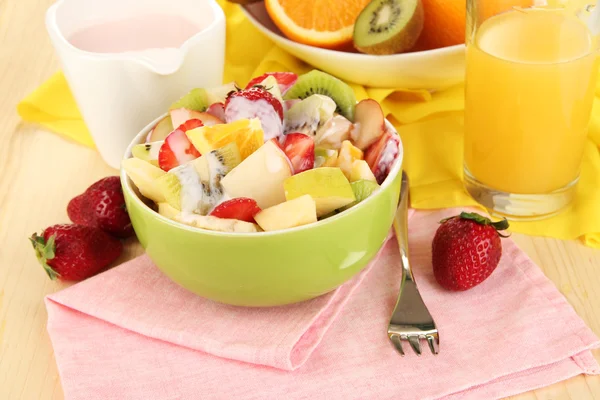 Nyttig fruktsallad med färsk frukt och bär i skål på servett på träbord närbild — Stockfoto