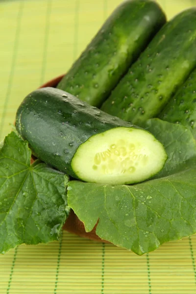 Tasty green cucumbers in wooden bowl, on bamboo mat background — Stock Photo, Image