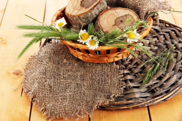 Many spikelets and chamomile on satin in basket on wooden background — Stock Photo, Image