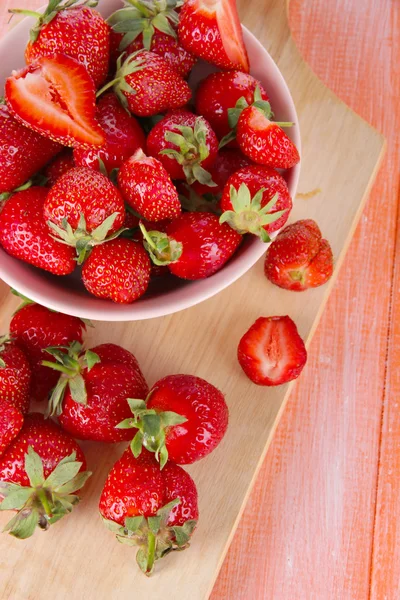 Strawberries in bowl on cutting board on wooden table — Stock Photo, Image