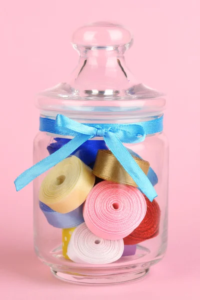 Glass jar containing various colored ribbons on pink background — Stock Photo, Image