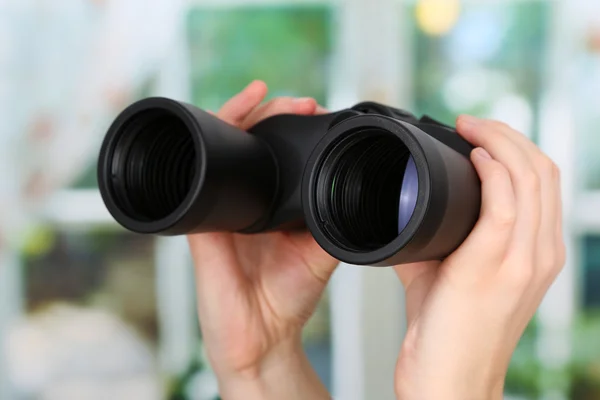 Black modern binoculars in hands on window background — Stock Photo, Image