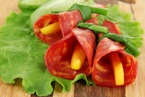 Salami rolls with paprika pieces inside, on wooden board — Stock Photo, Image