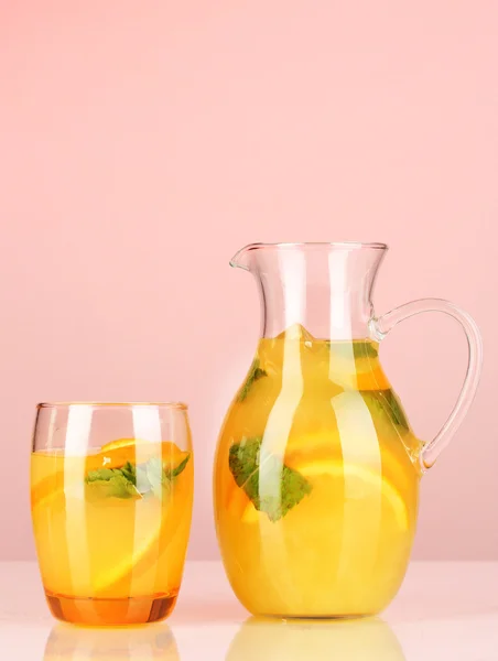 Orange lemonade in pitcher and glass on pink background — Stock Photo, Image