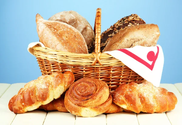 Composition with bread and rolls, in wicker basket on wooden table, on color background — Stock Photo, Image