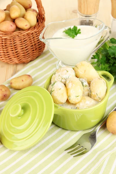 Tender young potatoes with sour cream and herbs in pan on wooden table close-up — Stock Photo, Image