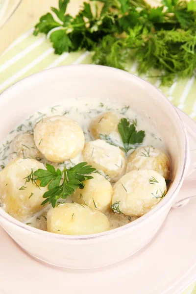 Tender young potatoes with sour cream and herbs in pan on wooden table close-up — Stock Photo, Image