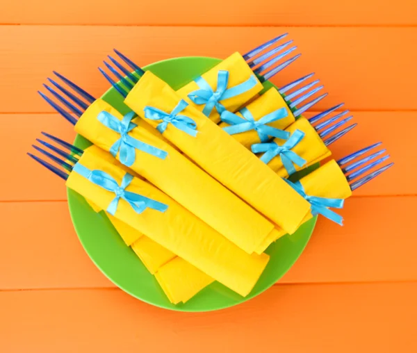Голубые пластиковые вилки, завернутые в салфетки из желтой бумаги, на фоне цвета дерева — стоковое фото
