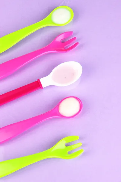 Colheres de cor e garfos para comida de bebê no fundo roxo — Fotografia de Stock