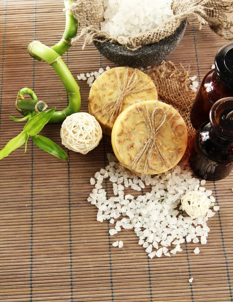 Handgemachte Seife, Flaschen und Meersalz auf grauer Bambusmatte — Stockfoto