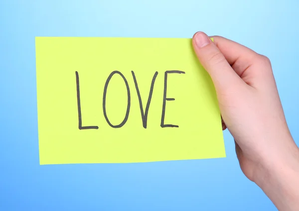Palabra de amor sobre papel trozo en mano sobre fondo azul — Foto de Stock