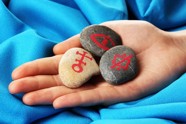 Fortune telling with symbols on stone in hand on blue fabric background — Stock Photo, Image