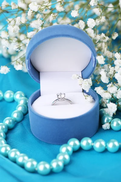 Kwiaty i pierścionek zaręczynowy na niebieski tkaniny — Zdjęcie stockowe