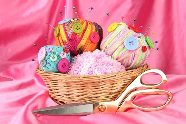Πολύχρωμα κουμπιά και πολύχρωμα μαλλί μπάλες σε ψάθινο καλάθι, σε χρώμα υφάσματος υπόβαθρο — Φωτογραφία Αρχείου