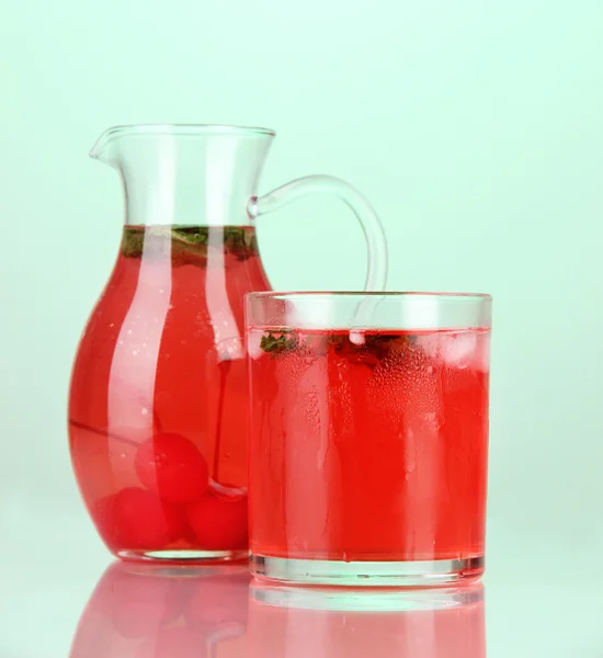 Вишневый напиток в кувшине и стакан на зеленом бэкграунде — стоковое фото