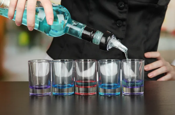 Barmen hand with bottle pouring beverage into glasses, on bright background — Stock Photo, Image